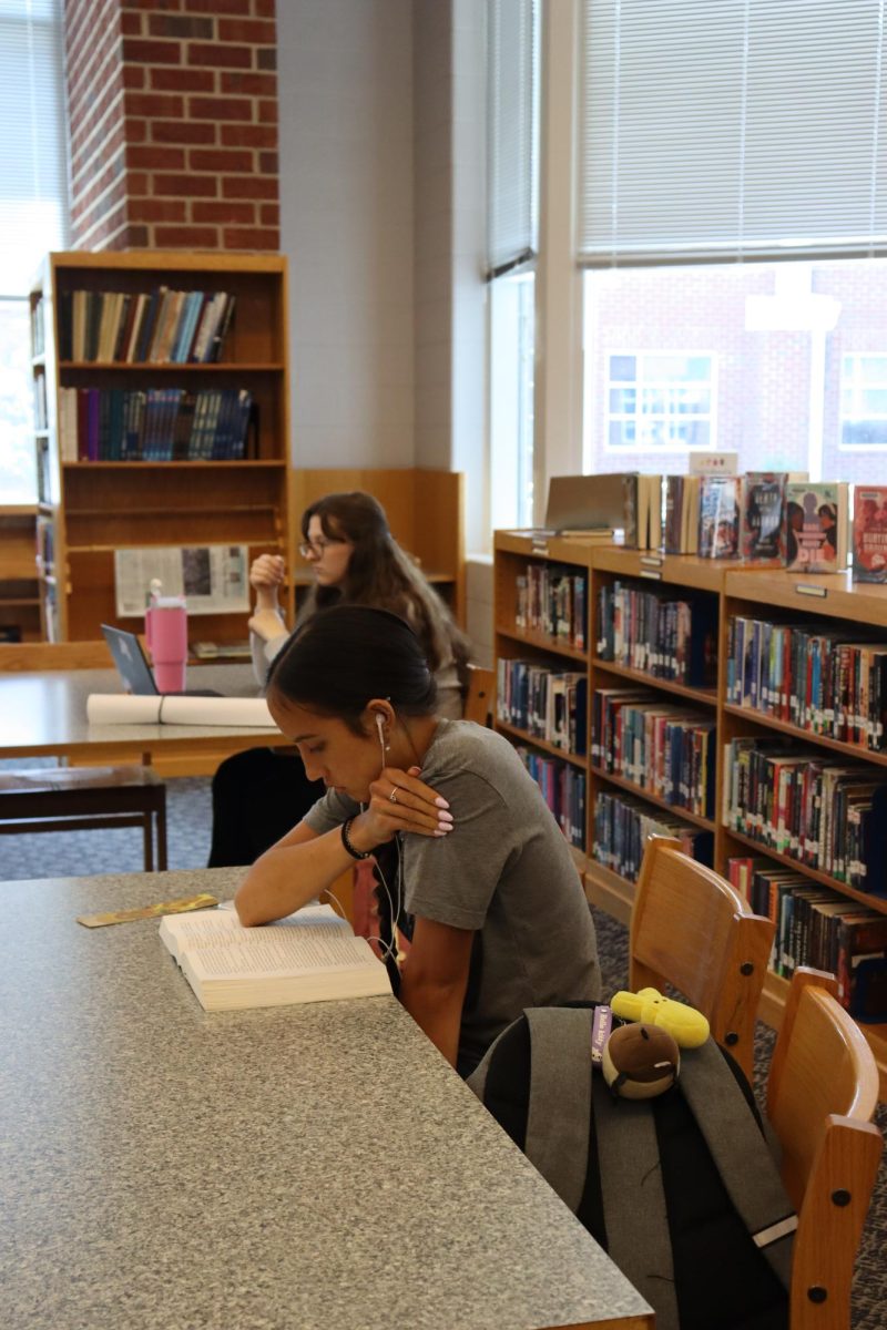Student focused on reading her book and listening to music. 