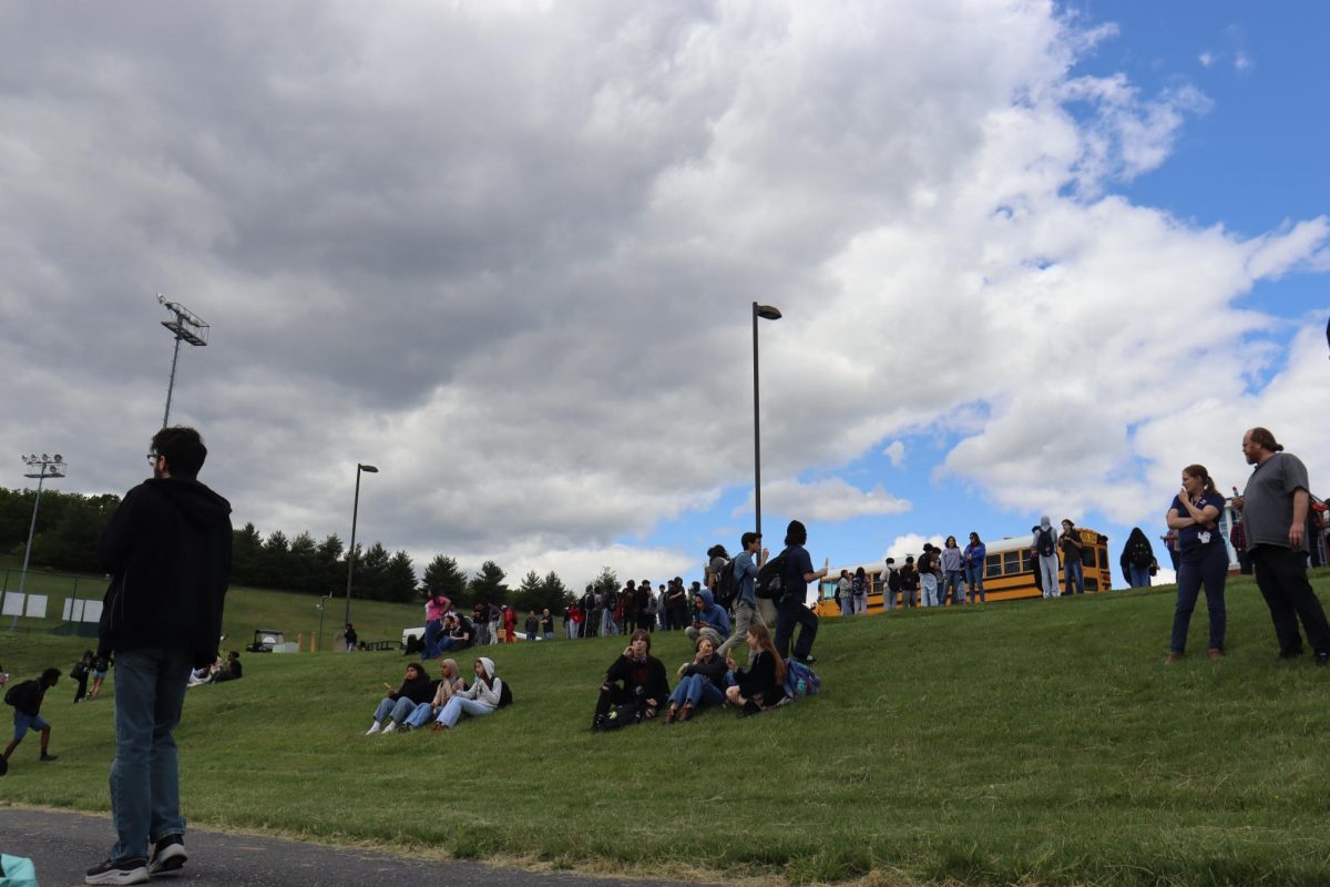 Students sit and talk on the hill as busses begin to pull up.