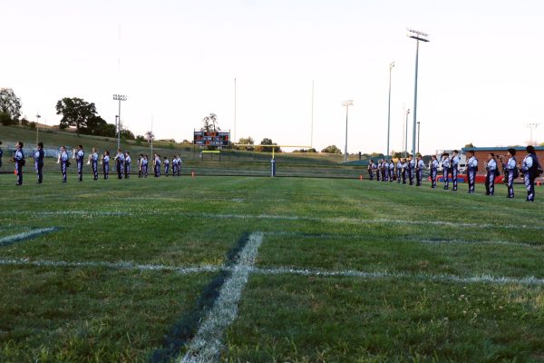 Band members stand in a line on the field.