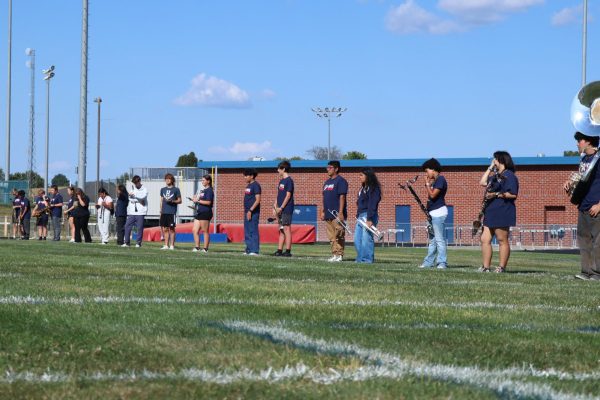 Band members stand in a line on the field.