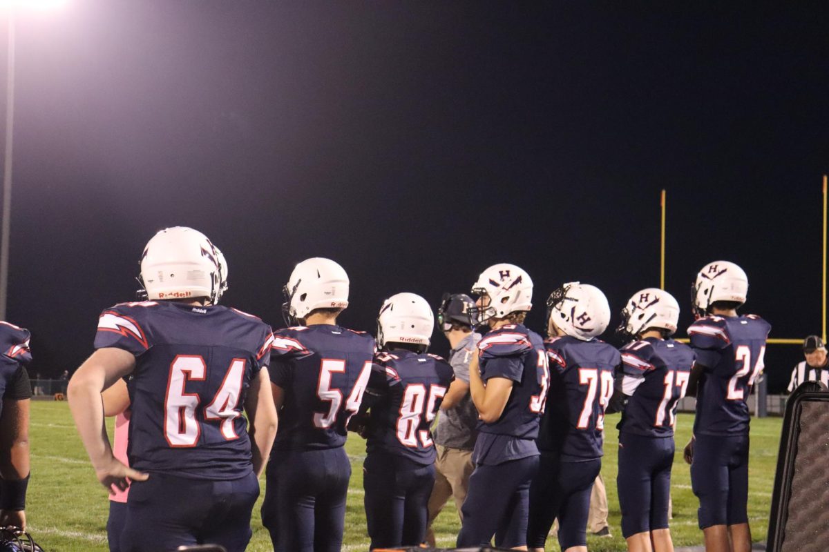 Varsity football team standing on the side of the field watching and cheering on there teammates. 